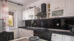 Une cuisine moderne avec des meubles blancs, un pare-feu noir et une table à manger en verre.