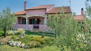Une maison à la façade rose, agrémentée d’éléments en pierre et surmontée d’un toit recouvert de tuiles.