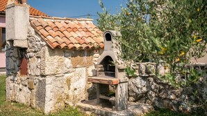 Un four extérieur en pierre, doté d’un toit en tuiles, entouré de murs de pierre et de végétation.