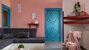 Un salon avec un canapé d’angle, une petite table sur laquelle est posée une plante, une porte bleue et une étagère avec des plantes en pot.