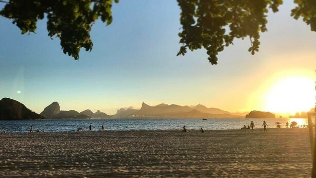 A beach scene with people, a sunset, and distant mountains. - Studio (RJ)