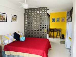 Quarto com cama, escrivaninha e cozinha compacta.
