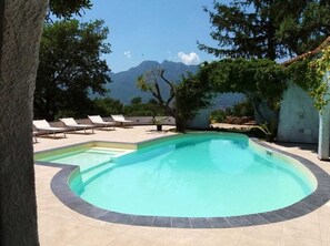 A swimming pool with lounge chairs, surrounded by trees and a mountain view.