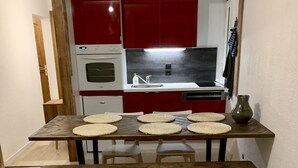 Zona de menjador amb taula i banc de fusta, cuina al fons amb armaris vermells i forn blanc.