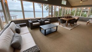A spacious room with a large window overlooking a body of water, furnished with a sofa, chairs, and a dining table.
