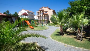 A residential area with a playground, a curved gravel path, and a large building with balconies. - Vacation apartment Šanić Lopar 543a (Lopar)