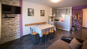 A compact living space with a dining area, kitchenette, and a flat-screen TV mounted on a stone wall. - Vacation apartment Šanić Lopar 543a (Lopar)