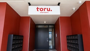 A modern building entrance with a sign reading 'toru. APARTMENTS' and a dark door. - Remarkables Park: Modern Apartment with Parking (Queenstown)