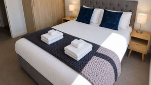 A hotel room with a bed, two bedside tables, a wardrobe, and a lamp. - Remarkables Park: Modern Apartment with Parking (Queenstown)