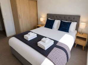A hotel room with a bed, two bedside tables, a wardrobe, and a lamp. - Remarkables Park: Modern Apartment with Parking (Queenstown)