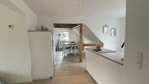 Eine moderne Küche mit weißen Schränken, Holzbalkendecke und einem Essbereich im Hintergrund.