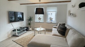 Ein modernes Wohnzimmer mit einem beigefarbenen Sofa, einem Glastisch und einem an der Wand montierten Fernseher.