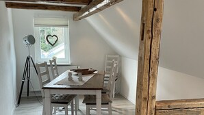 Ein Essbereich mit einem Holztisch und Stühlen, einem Stativ mit einer Kamera und einem herzförmigen Dekorationsobjekt am Fenster.