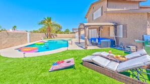 A backyard with a swimming pool, a covered patio area, and outdoor seating.