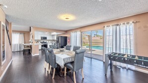 A spacious living room with a foosball table, a dining area with a table and chairs, and a kitchen in the background.