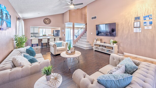 A spacious living room with a large TV, comfortable sofas, a coffee table, and a staircase leading to the upper floor.