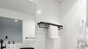 Een moderne badkamer met een wit wastafel, spiegel en toilet. Op het aanrecht staan twee flessen handzeep en lotion, en boven het toilet is een handdoekhouder.