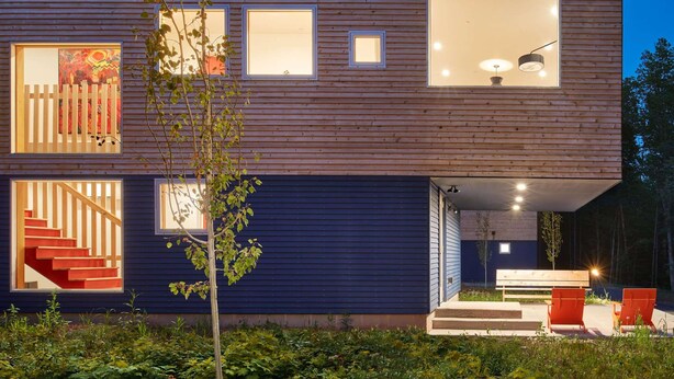 Een modern huis met twee verdiepingen, een houten gevel, grote ramen en een zichtbare trap.