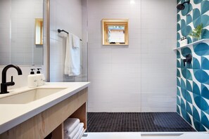 Een moderne badkamer met een grote spiegel, een wastafel met handzeep, een handdoekrek, een douche met een zwarte vloer en een raam met uitzicht.