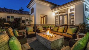 An outdoor seating area with wicker furniture and a central fire feature. - Villa Del Sol - 3 Suites w/ Pool, Spa, Firepit (La Quinta)