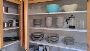 Una cocina con alacenas abiertas que exhiben diversos utensilios de cocina, incluyendo ollas, sartenes y equipo para preparar café.