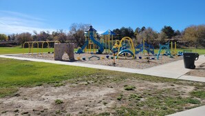 Un parque infantil con diversas estructuras de juego, una zona cubierta y un contenedor de basura.