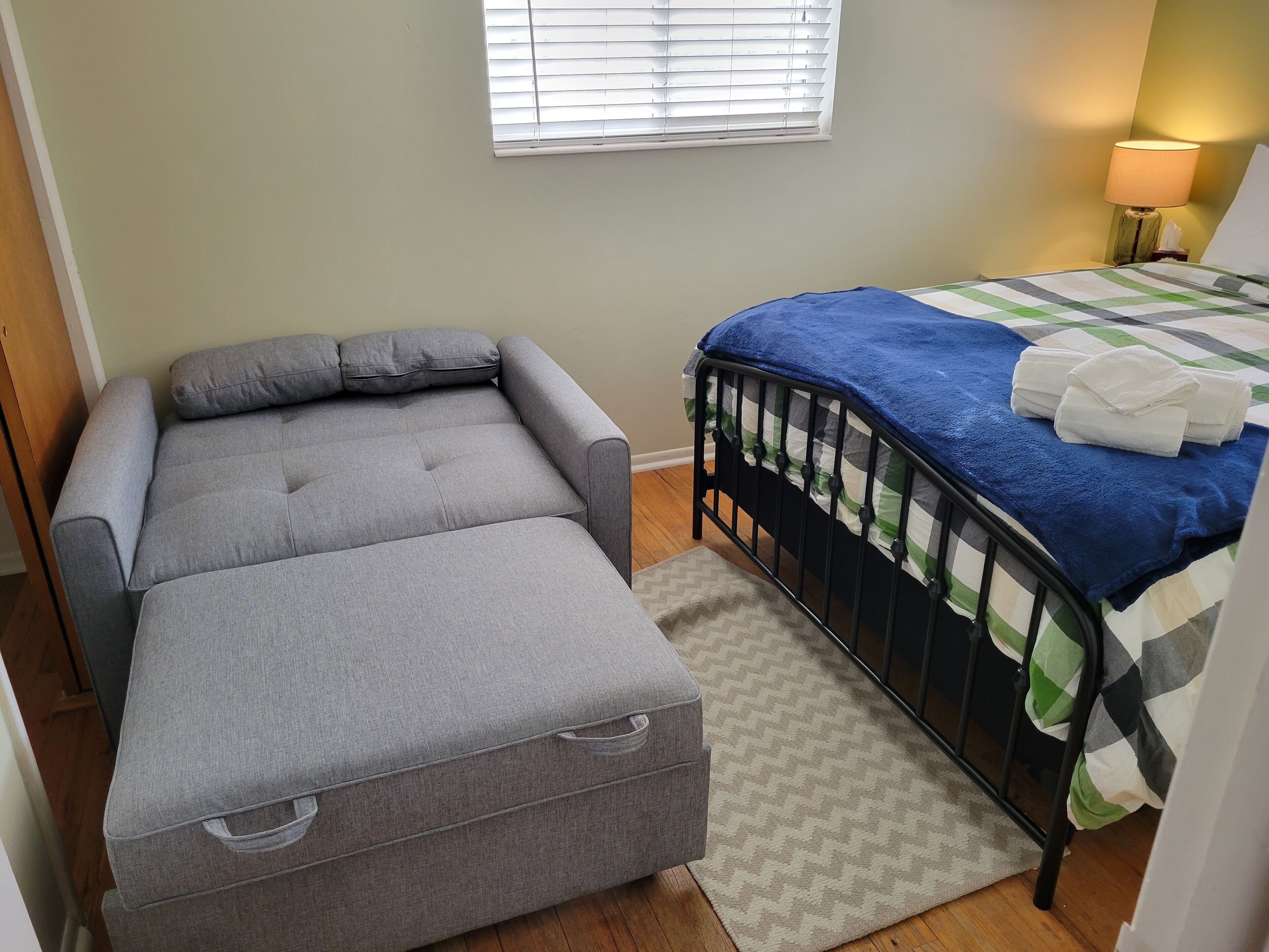 Una camera da letto con un divano grigio, un letto con coperta blu e una lampada da comodino.