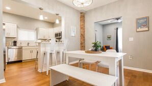 A modern kitchen with white cabinetry, a central island, and a dining area with a bench. - Backyard Oasis - FIRE PIT - Walk to Brewery/Coffee (Kansas City)