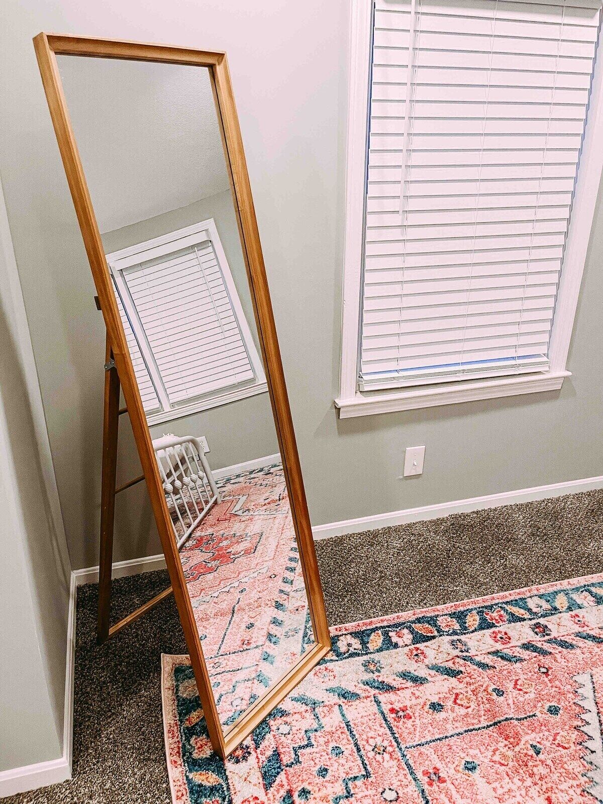 Une pièce avec un grand miroir, une fenêtre avec des stores, un tapis à motifs et un radiateur.