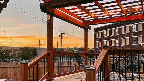 A wooden staircase leading to a covered outdoor area with a view of buildings in the background. - Backyard Oasis - FIRE PIT - Walk to Brewery/Coffee (Kansas City)