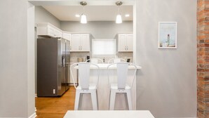 A modern kitchen with white cabinets, a stainless steel refrigerator, and a white dining table with chairs. - Backyard Oasis - FIRE PIT - Walk to Brewery/Coffee (Kansas City)