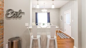 A dining area with a white table and chairs, a chandelier, and a wall sign that reads "Eat." - Backyard Oasis - FIRE PIT - Walk to Brewery/Coffee (Kansas City)