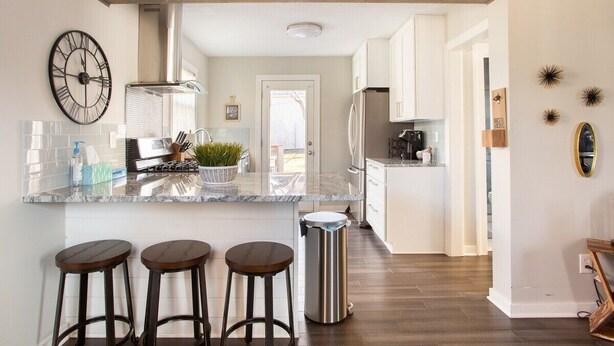 A modern kitchen with a central island, bar stools, and a stainless steel trash can. - West Plaza House in the heart of KC (Kansas City)