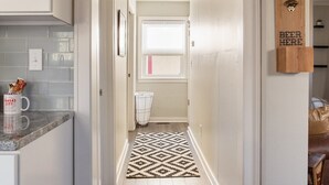 A narrow hallway with a kitchen area on the left, a window with a view, and a wooden sign on the right. - West Plaza House in the heart of KC (Kansas City)