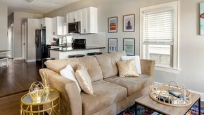 A modern living room with a beige sofa, a glass coffee table, and a kitchen in the background.