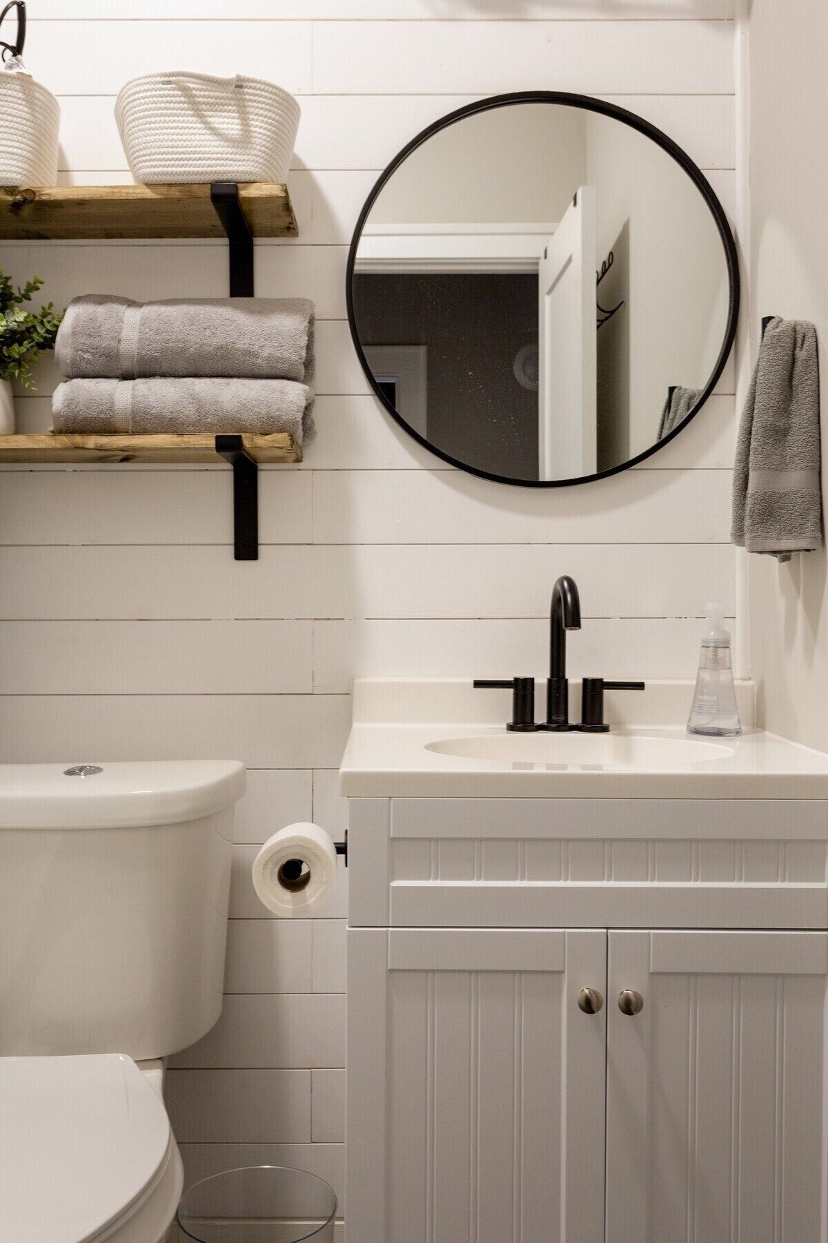 Une salle de bain comprenant des toilettes, un lavabo avec un miroir au-dessus, et une étagère avec des serviettes.