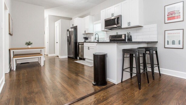A modern kitchen with white cabinets, stainless steel appliances, and a black trash can.