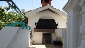 Un pequeño patio exterior con suelo de baldosas, una parrilla negra y una pared blanca con una ventana.