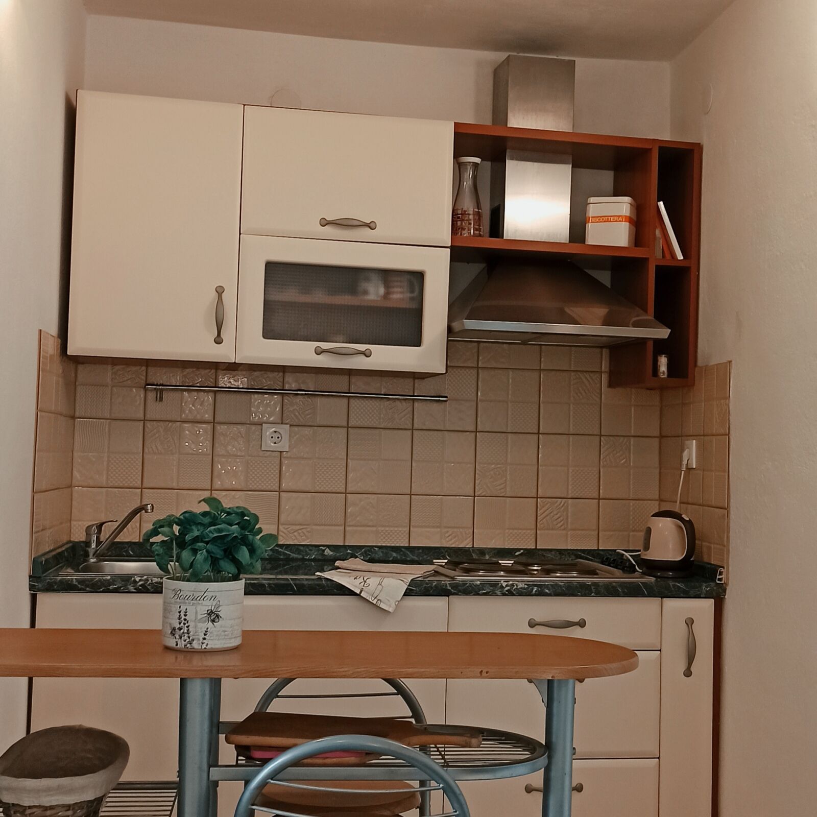 A compact kitchen with white cabinets, a microwave, and a small shelf with items.