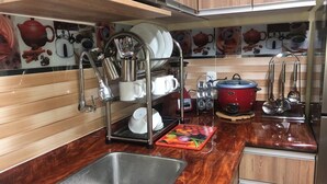Eine Küche mit Spüle aus Edelstahl, einem Geschirrgestell, einem roten Slow Cooker und einer Mikrowelle.