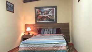Ein Schlafzimmer mit Holzboden, einem Bett mit gestreifter Bettdecke, einem Nachttisch mit Lampe und einem gerahmten Bild an der Wand.