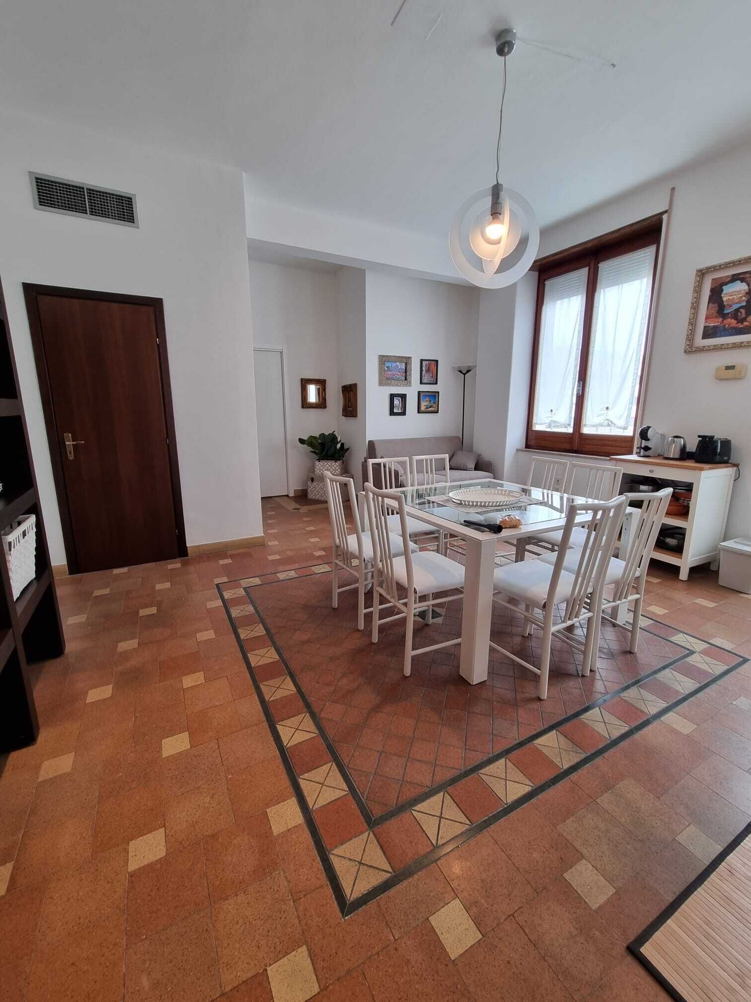A spacious living area with a dining table surrounded by chairs, a kitchen area with a stove and cabinets, and a large window with curtains.
