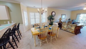 A dining area with a table set for four, surrounded by chairs. There is a chandelier above the table, and a plant is visible in the background. - Magnolia Pointe Retreat with Pool & Golf Views | Magnolia Point Unit 201 (Myrtle Beach)