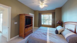 A bedroom with a bed, a wooden TV stand, a ceiling fan, and a window with curtains. - Magnolia Pointe Retreat with Pool & Golf Views | Magnolia Point Unit 201 (Myrtle Beach)