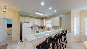 A modern kitchen with white cabinets, a central island with bar stools, a refrigerator, microwave, and a sink. - Magnolia Pointe Retreat with Pool & Golf Views | Magnolia Point Unit 201 (Myrtle Beach)