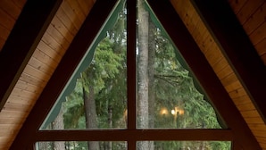 Una baita con un'ampia finestra che si affaccia su una zona boschiva. All'interno, un pavimento in legno con mobili da esterno.