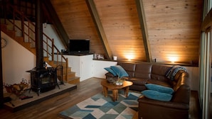 Un accogliente soggiorno mansardato con soffitto in legno, camino, divano e televisore.