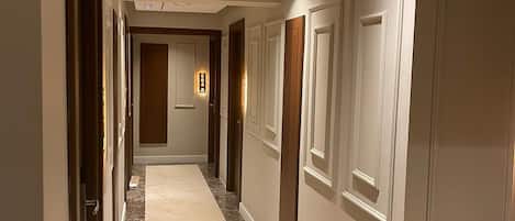 A hallway with a marble floor, white walls, and doors with wooden panels.