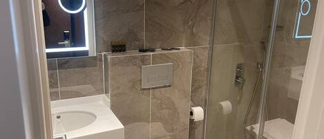 Un baño moderno con cabina de ducha de vidrio, un lavabo blanco y un inodoro.