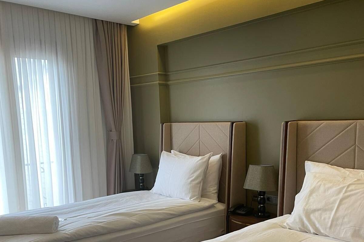 Een hotelkamer met twee bedden, een nachtkastje met een lamp en een raam met gordijnen.